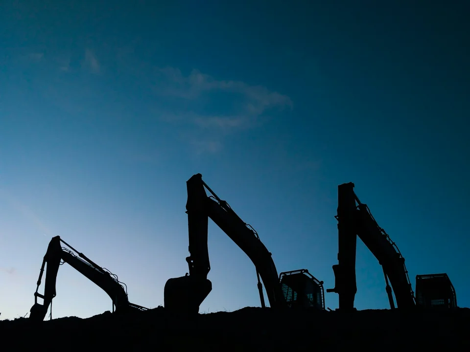 Three excavators silhouetted against a deep blue sky
